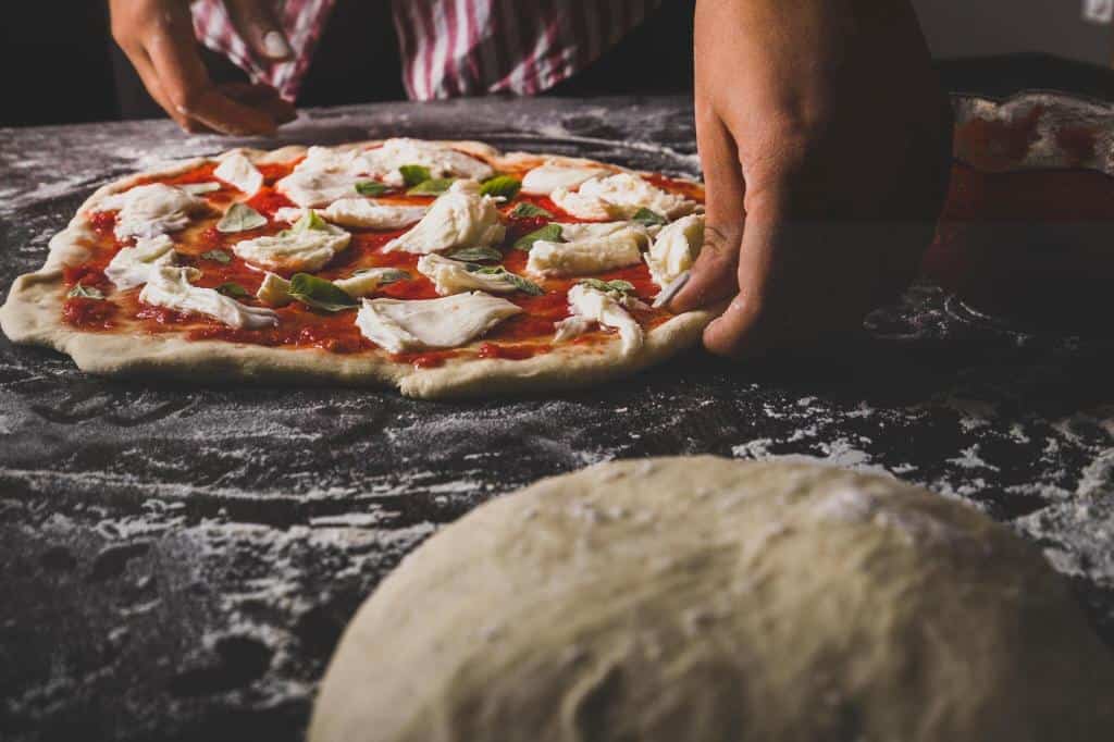 a chef preparing a cheese and basil pizza
