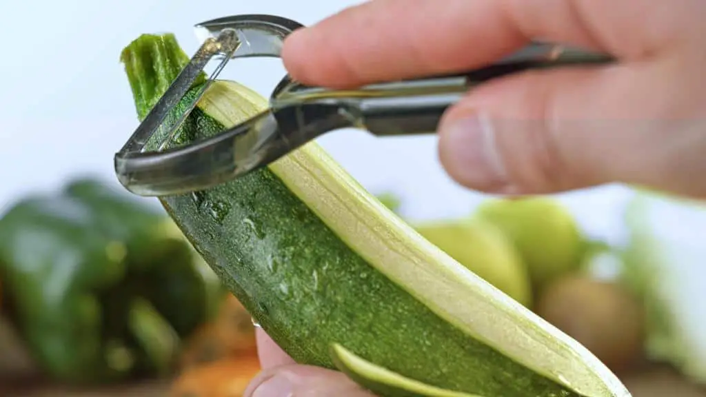 hand peeling a zucchini skin with a peeler