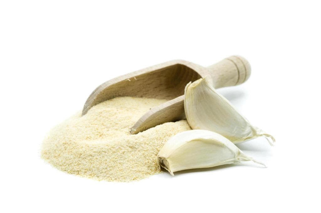 a pile of garlic powder with scoop and garlic cloves