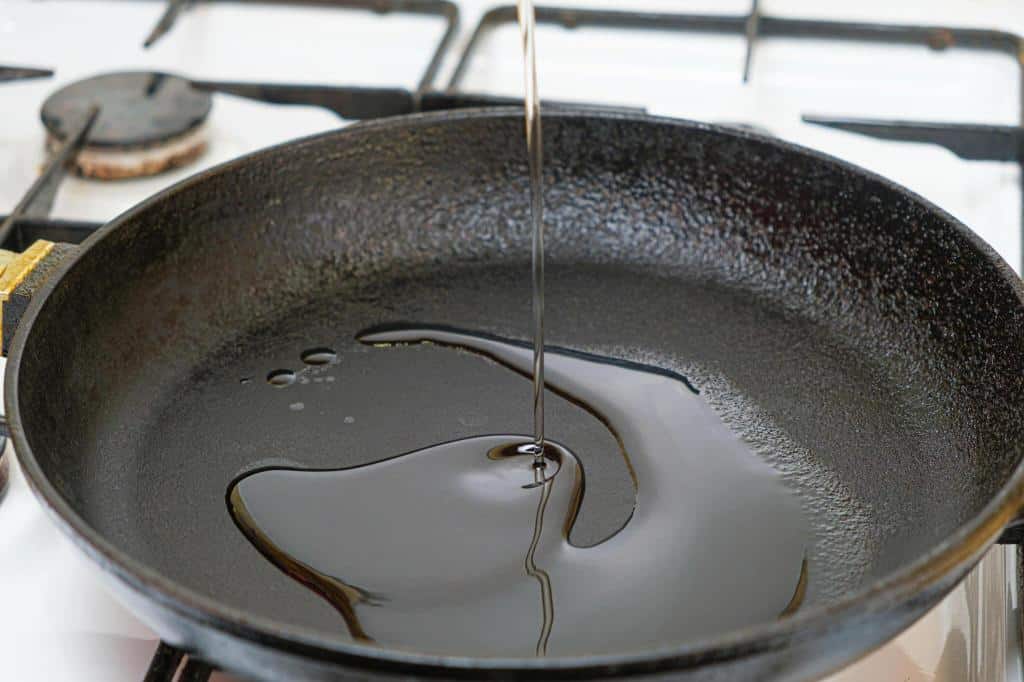 pouring vegetable oil into-a-cast iron heated frying pan