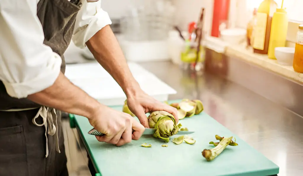 cutting artichokes for dinner preparation man cooking inside restaurant kitchen