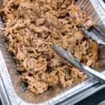 a large aluminum roasting pan full of seasoned pulled pork