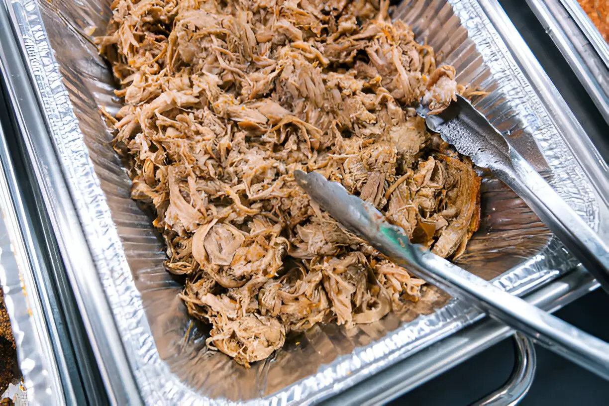 a large aluminum roasting pan full of seasoned pulled pork