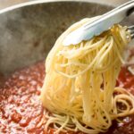 spaghetti being put in the pan-with hot bolognese sauce
