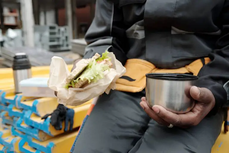 worker holding cup with hot tea and sandwich
