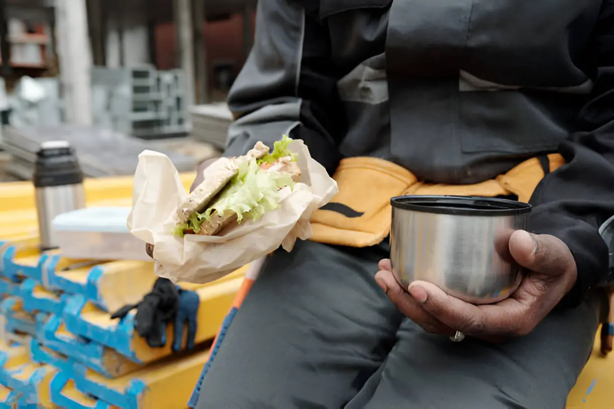 worker holding cup with hot tea and sandwich